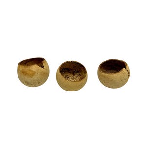 May include: Three small, round, beige-colored bowls with rough, textured exteriors. The interiors of the bowls are a darker, speckled brown. Each bowl has a unique opening at the top, suggesting they are handmade and natural.