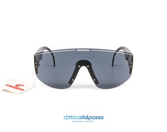 May include: Black Carrera sunglasses with a white stripe across the top of the frame. The sunglasses have a wraparound design and gray lenses.