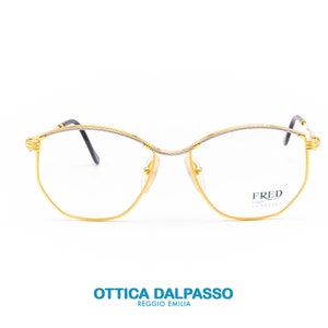 Op de afbeelding: Gouden metalen bril met een zilveren draadframe. De bril heeft een cat-eye vorm en de merknaam "FRED PARIS" is gedrukt op de rechter lens.