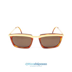 Puede incluir: Un par de gafas de sol cuadradas de color marrón y dorado. Las lentes son marrones y las patillas son doradas.