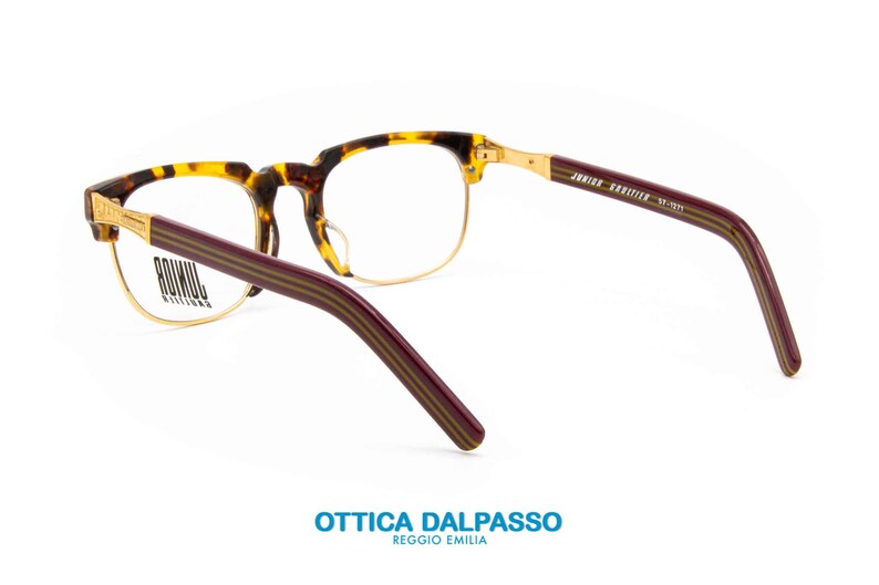 May include: Tortoise shell and gold-rimmed eyeglasses with burgundy temples featuring a striped pattern. The arms are labeled "JUNIOR KRIZIA" and "JF-1221".