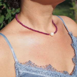 Op de afbeelding: Een delicate ketting met een enkele parel hanger. De ketting is gemaakt van kleine, gefacetteerde, roze kralen.