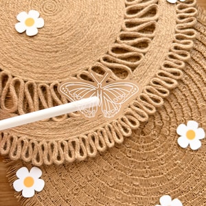 May include: Two round jute placemats with a decorative edge are shown in a close-up. A white butterfly sticker and several white daisy stickers with yellow centres are scattered across the placemats. A white stylus is also visible.