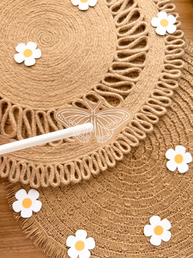 May include: Two round jute placemats with a decorative edge are shown in a close-up. A white butterfly sticker and several white daisy stickers with yellow centres are scattered across the placemats. A white stylus is also visible.