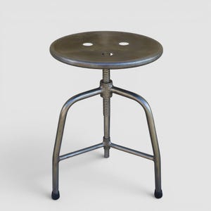 Könnte beinhalten: Verstellbarer Hocker im industriellen Stil mit runder, perforierter Sitzfläche. Der Sitz wird von einer Gewindesäule und drei gebogenen Beinen getragen. Das Metall hat eine abgenutzte, silberne Oberfläche. Minimalistisches Design.