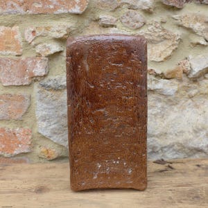 Puede incluir: Un jarrón de cerámica marrón rectangular y alto con una superficie texturizada.
