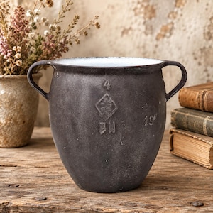 May include: A dark charcoal grey metal pot with two side handles and a white interior. The exterior features embossed markings including the number 4, a diamond shape with a symbol inside, the letters BH, and the number 19.