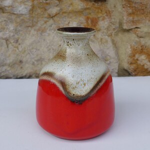 Può includere: Un vaso in ceramica con base bulbosa e collo stretto. La parte inferiore è di un rosso vivido e solido, mentre la sezione superiore e il bordo presentano uno smalto color crema maculato con un motivo a goccia marrone scuro che separa le zone.