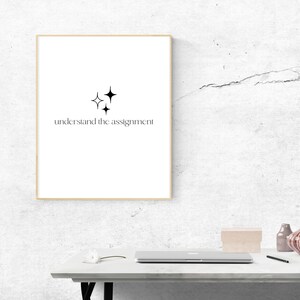 K&ouml;nnte beinhalten: Ein gerahmter Druck mit einem minimalistischen Design mit drei schwarzen Sternen und dem Text "understand the assignment". Der Druck h&auml;ngt an einer wei&szlig;en, strukturierten Wand.