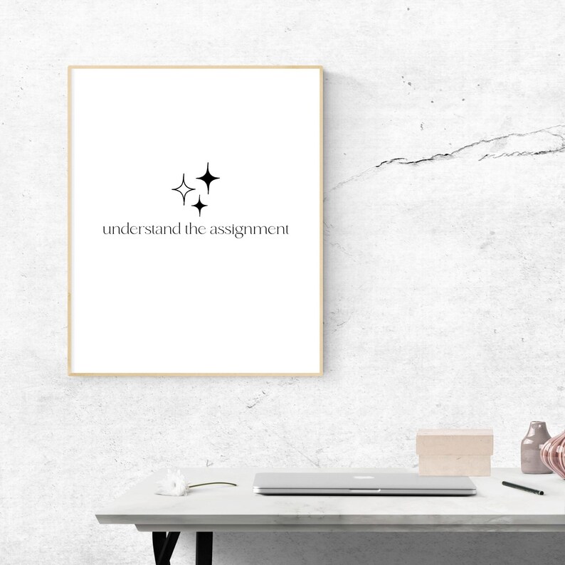 K&ouml;nnte beinhalten: Ein gerahmter Druck mit einem minimalistischen Design mit drei schwarzen Sternen und dem Text "understand the assignment". Der Druck h&auml;ngt an einer wei&szlig;en, strukturierten Wand.