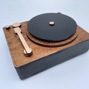 K&ouml;nnte beinhalten: Ein Holz-Plattenspieler mit einer schwarzen Schallplatte, einem Holzarm und einem schwarzen Sockel.