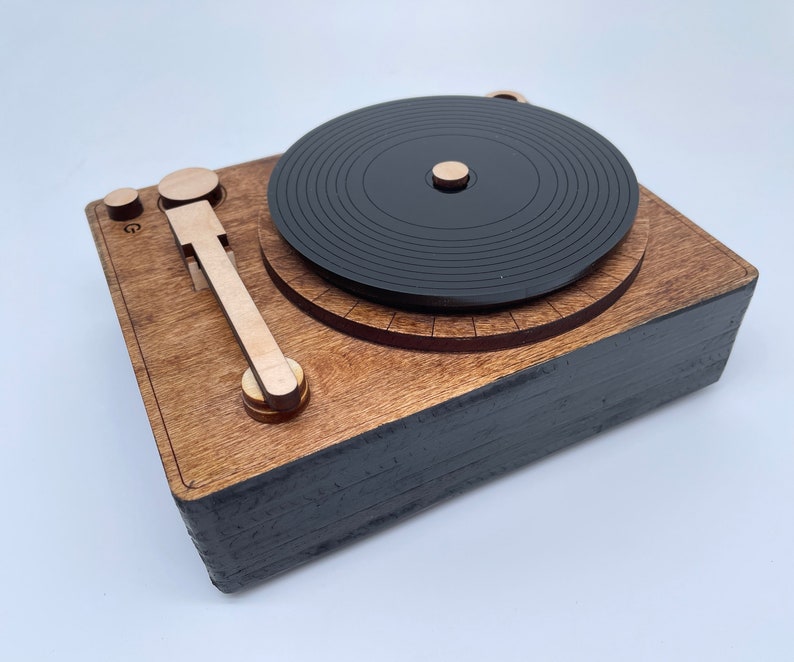 K&ouml;nnte beinhalten: Ein Holz-Plattenspieler mit einer schwarzen Schallplatte, einem Holzarm und einem schwarzen Sockel.