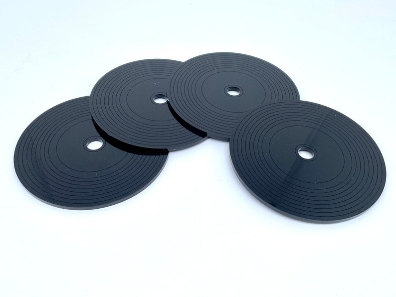 K&ouml;nnte beinhalten: Vier schwarze Untersetzer in Form von Schallplatten mit konzentrischen Kreisen und einem kleinen Loch in der Mitte.