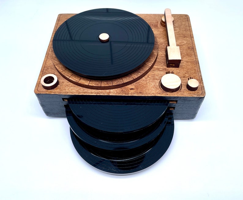 K&ouml;nnte beinhalten: Ein Holz-Plattenspieler mit einem schwarzen Plattenteller und einem Stapel von vier schwarzen Vinylplatten. Der Plattenspieler hat einen Holztonarm und einen Holzknopf.