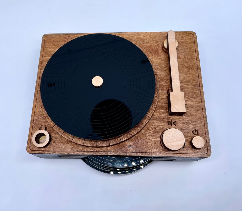 K&ouml;nnte beinhalten: Ein Holz-Plattenspieler mit einer schwarzen Schallplatte, einem Lautst&auml;rkeregler und einem Ein-/Ausschalter. Der Plattenspieler ist aus Holz und hat einen Vintage-Look.
