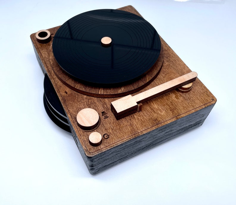 K&ouml;nnte beinhalten: Ein Holz-Plattenspieler mit einer schwarzen Schallplatte, einem Holzarm und einem Holzsockel. Der Plattenspieler hat eine braune Beize und eine schwarze Oberfl&auml;che.