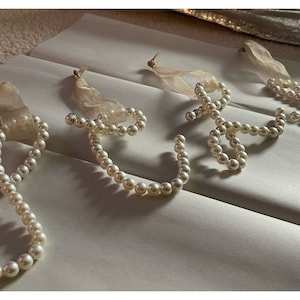 May include: Five white pearl ornaments shaped into letters, each with a white ribbon attached.