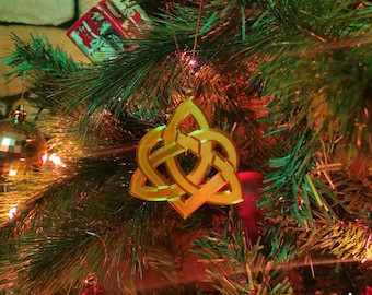 May include: A gold Celtic knot ornament hanging on a Christmas tree with red and green decorations. The ornament is a traditional symbol of love, friendship, and unity.