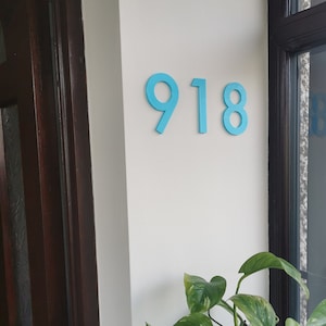 May include: A close-up of a house number sign with the number 918 in bright blue on a white wall.