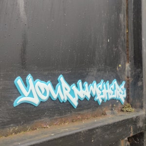 a 3d printed graffiti tag that says 'your name here' in white with a blue background