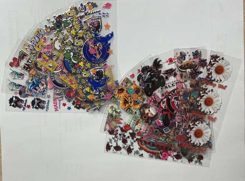 May include: A collection of colorful stickers featuring various designs, including cartoon characters, flowers, and logos. The stickers are arranged in a fan shape on a white background.