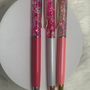 May include: Three glitter pens with pink, white, and gold barrels. The pens have clear bodies filled with colorful glitter that moves when the pen is shaken.