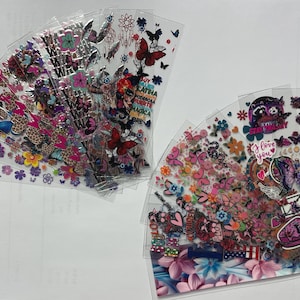 May include: A set of 10 clear plastic sheets with colorful butterfly, flower, and heart stickers. The stickers are arranged in a fan shape and feature various designs, including butterflies, flowers, hearts, and the words "Stay Strong" and "I Love You".