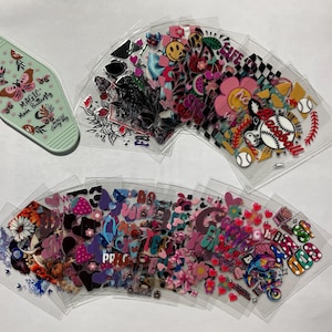 May include: A set of colorful stickers featuring various designs, including hearts, stars, smiley faces, and words like "life" and "good". The stickers are arranged in a fan shape on a white surface.