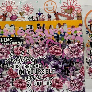 Pu&ograve; includere: Una collezione di adesivi a tema floreale con vari disegni e testo. Gli adesivi presentano fiori rosa e viola, faccine sorridenti, matite e le frasi "darling", "Just Believe in Yourself" e "I am a Teacher, Sunflower."