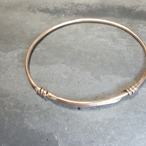 Puede incluir: Un brazalete simple de oro con un diseño trenzado en el cierre.