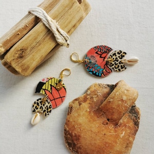 Puede incluir: Un par de pendientes coloridos con un diseño geométrico. Los pendientes están hechos de resina y presentan un estampado de leopardo, un patrón floral y un pequeño amuleto de concha.