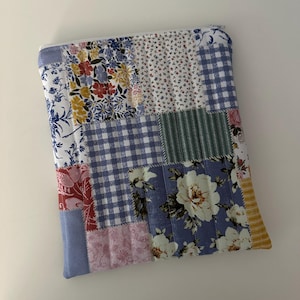 May include: A patchwork fabric pouch with a zipper closure. The pouch is made of different floral and checkered patterns in shades of blue, pink, yellow, and green.