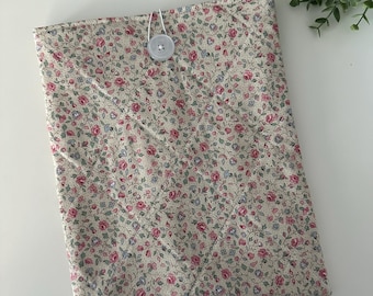 May include: A cream-colored fabric pouch with a floral pattern featuring pink and blue flowers. The pouch has a white button closure.