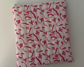 Op de afbeelding: Een witte ritszak met een roze en wit gestikt patroon van linten en strikken.