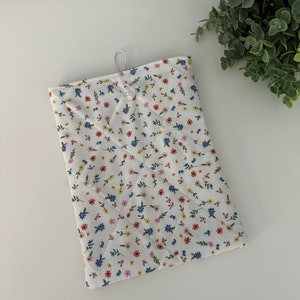Op de afbeelding: Een witte gewatteerde tablethoes met een bloemenpatroon in rood, blauw en geel. De hoes heeft een knoopsluiting en een lus aan de bovenkant. Het bloemenpatroon staat tegen een witte achtergrond.