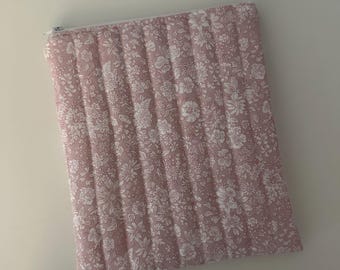 May include: A pink quilted zippered pouch with a white floral pattern.