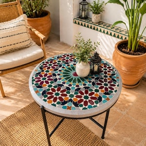 May include: A round side table featuring a mosaic tile top with a geometric star pattern in shades of deep red, teal, dark blue, and orange. The table has a light gray border and is supported by a thin black metal frame with four legs.