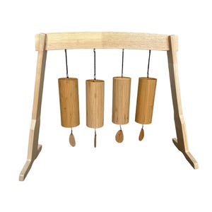Op de afbeelding: Een houten standaard met vier hangende bamboe-klokken. De klokken hangen aan de standaard met zwarte koorden en hebben een natuurlijke houten afwerking.
