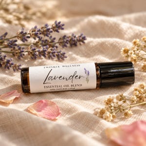 May include: A dark amber glass roller bottle with a black cap and a white label reading TWINKLE WELLNESS Lavender ESSENTIAL OIL BLEND 100% NATURAL | 10 ml, featuring a small lavender illustration, positioned horizontally.
