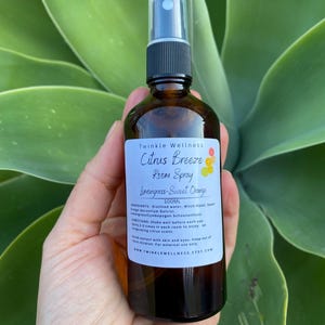 May include: A brown glass bottle with a black spray nozzle. The bottle is labeled "Twinkle Wellness Citrus Breeze Room Spray Lemongrass-Sweet Orange 100ML". The label also includes ingredients and directions for use.