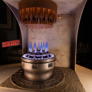 May include: A model of a sci-fi themed room with a circular platform with blue lights and a metal grate ceiling. The text "BRYAN MAKES DIORAMAS" is visible in the image.