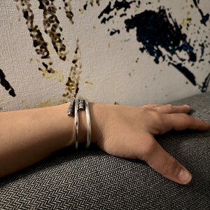 May include: A silver bangle bracelet with a textured design. The bracelet is made of multiple thin bands of metal that are twisted together.