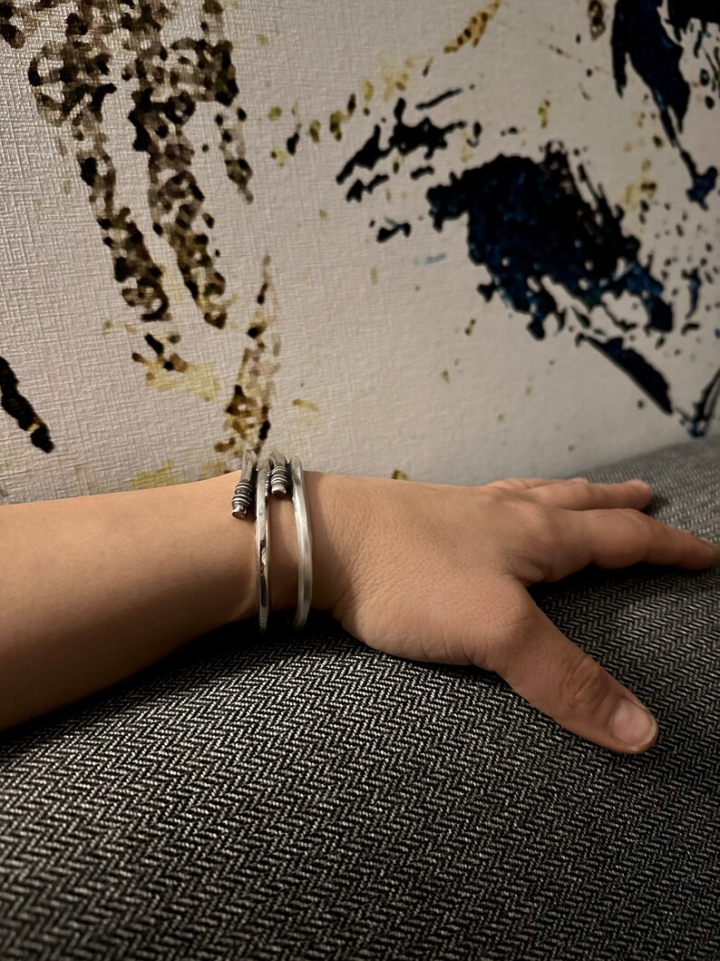 May include: A silver bangle bracelet with a textured design. The bracelet is made of multiple thin bands of metal that are twisted together.