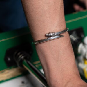 May include: A silver bracelet with a unique design featuring a curved band and a small, textured detail.