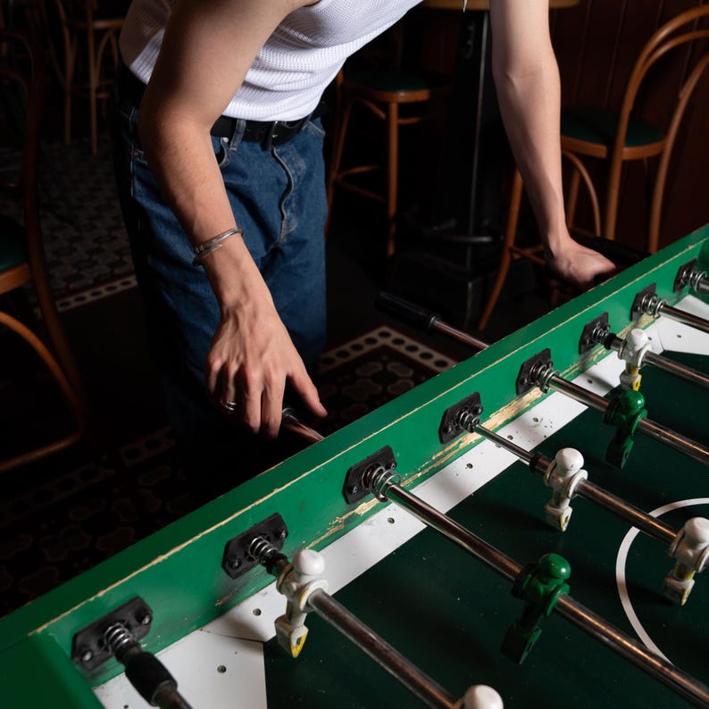 May include: A green table football game with silver rods and black and white players. The table is set up for a game with the players in position.