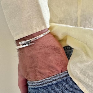 May include: A silver bracelet with a nail design and the words "minimal" and "toomuch" engraved on it.