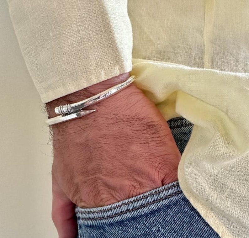 May include: A silver bracelet with a nail design and the words "minimal" and "toomuch" engraved on it.