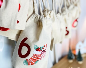 May include: A series of beige fabric advent calendar bags with red numbers and Christmas stocking illustrations. Each bag is tied with a drawstring and hangs from a string. The bags are decorated with a red number and a watercolor illustration of a Christmas stocking.
