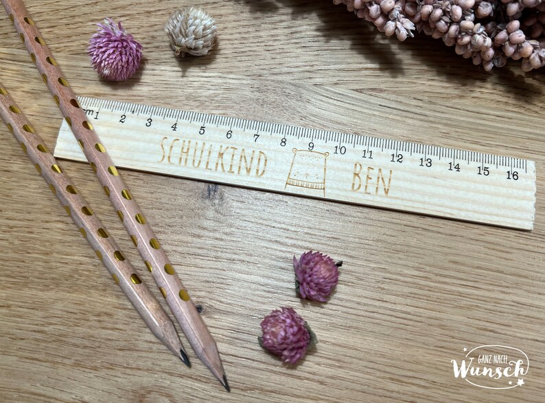May include: A wooden ruler with a cute bear illustration and the text "SCHULKIND BEN" engraved on it. The ruler is 16 inches long and has markings for each inch. Two pencils with gold polka dots are lying on a wooden surface next to the ruler.