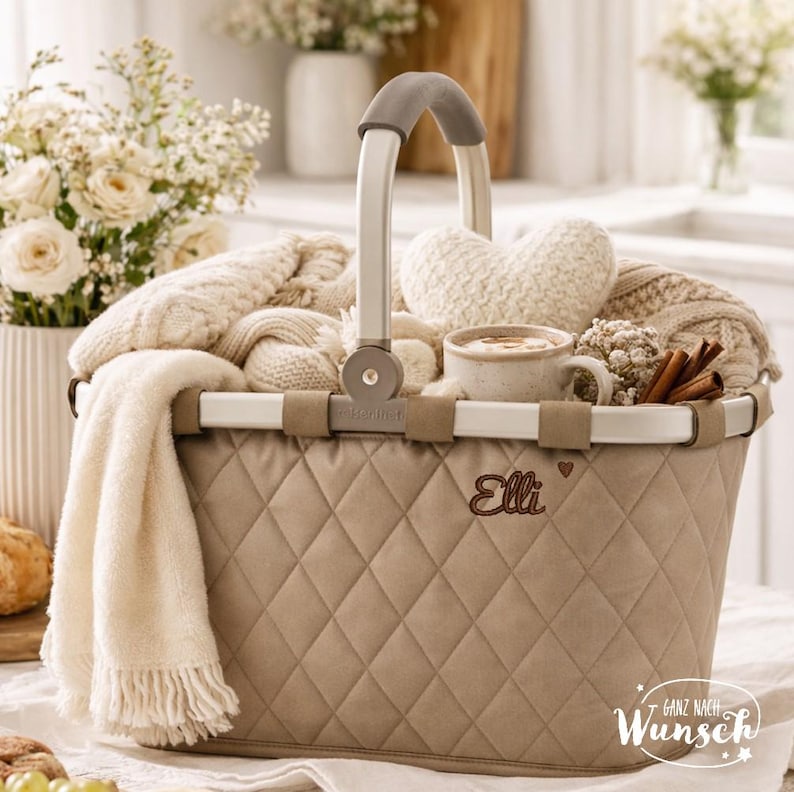 Pu&ograve; includere: Un cesto trapuntato beige con telaio in metallo argentato e manico grigio. Il cesto presenta il nome ricamato Elli con un piccolo cuore. All'interno ci sono coperte lavorate a maglia color crema, un cuscino a forma di cuore, una tazza e cannella.
